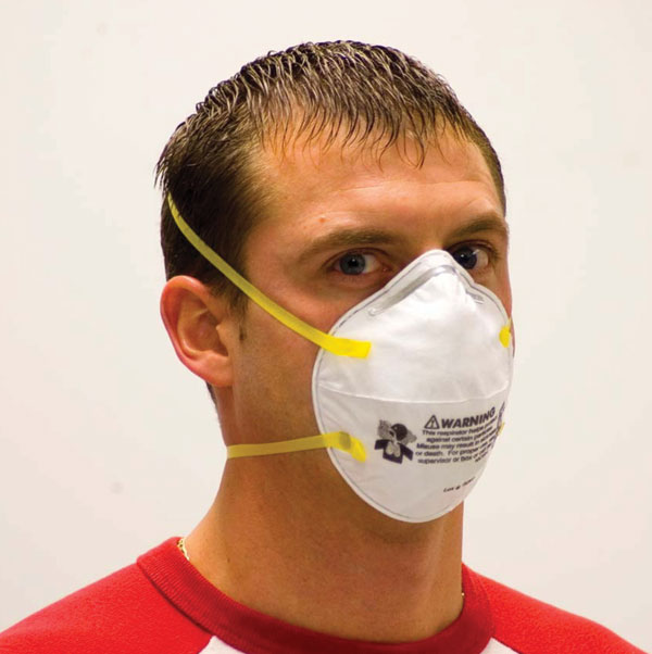 Properly donned disposable N95 filtering facepiece respirator. To be properly donned, the respirator must be correctly oriented on the face and held in position with both straps. The straps must be correctly placed, with the upper strap high on the head and the lower strap below the ears. For persons with long hair, the lower strap should be placed under (not over) the hair. The nose clip must be tightened to avoid gaps between the respirator and the skin. Facial hair should be removed before donning. Photo used with permission.