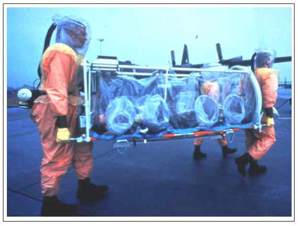Aeromedical isolation team members in field-protective suits equipped with battery-powered HEPA-filtered respirators transporting the stretcher isolator, a light-weight unit designed for initial patient retrieval. The team trains on several types of military aircraft, including the C-130 transport shown in the background.