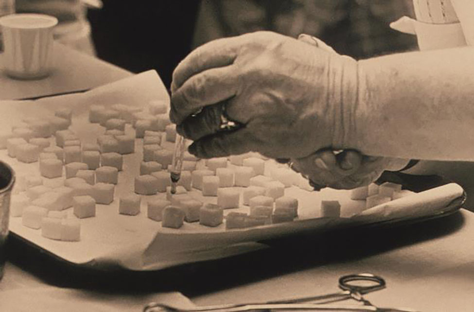 This historic 1975 photograph shows a laboratory technician preparing doses of polio vaccine by placing a liquid droplet of the vaccine upon each of these sugar cubes, which would subsequently be ingested orally by each recipient. Photo: Public Health Image Library, CDC, 1975